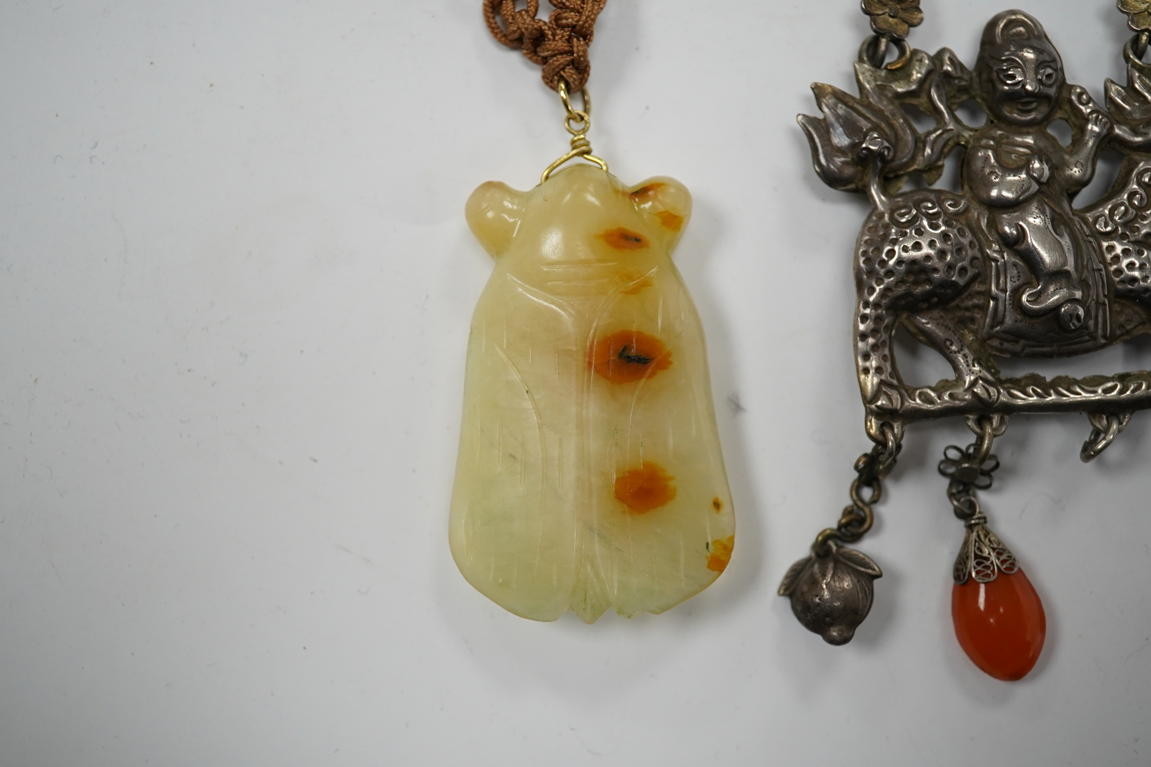 A Chinese celadon and russet jade cicada pendant on cording and a silver and stone mounted chain and pendant of boy riding a qilin, cicada 5.5cm long (2). Condition - tip of cicada wing chipped and on silver pendant one